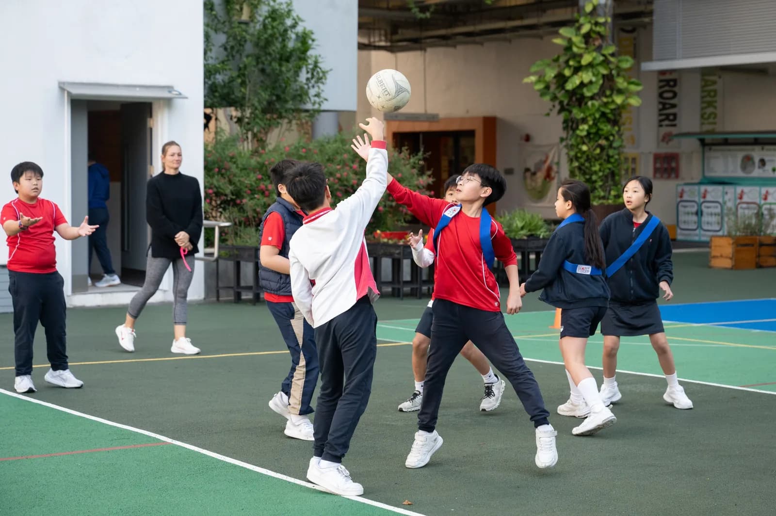 九龙小学学生在校园球场上跳起争抢无挡板篮球，老师在旁观看