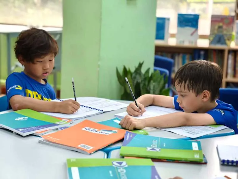 两名小学生在图书角旁的桌前练习书写