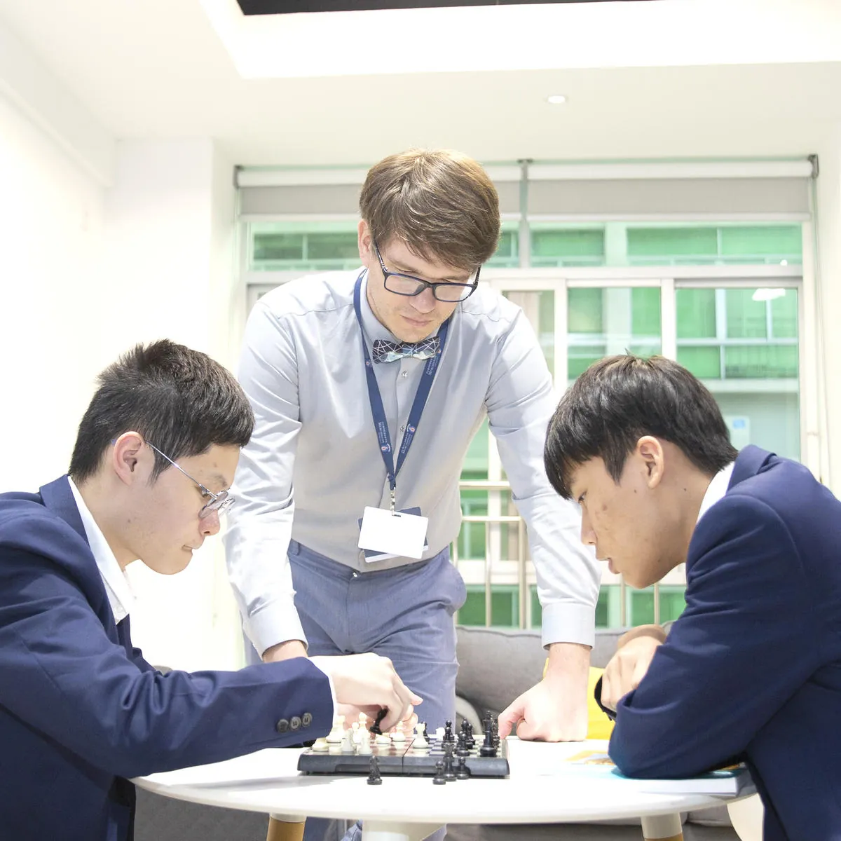 寄宿楼公共区里两名中学生下国际象棋，老师俯身观看